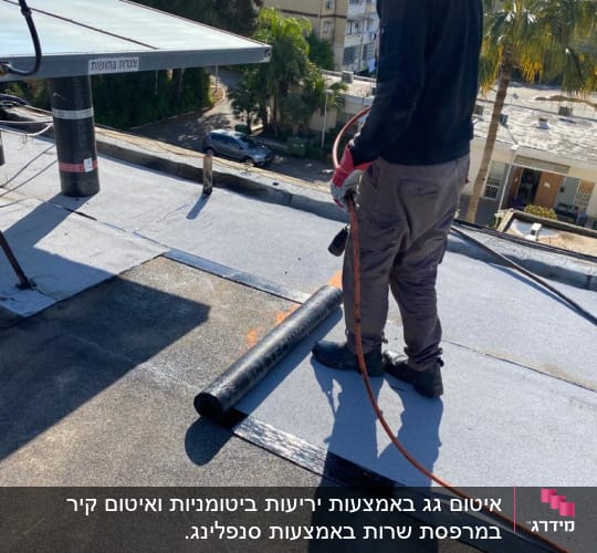 אדם עובד על גג עם יריעות ביטומניות